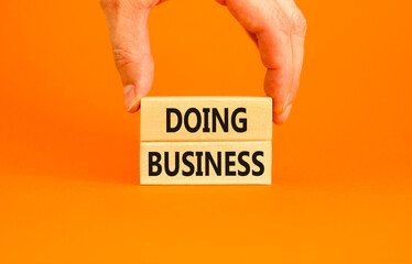 Doing business symbol. Concept words Doing business on beautiful wooden block. Beautiful orange table orange background. Businessman hand. Business, motivational Doing business concept. Copy space.