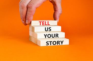 Tell us your story symbol. Concept word Tell us your story on beautiful wooden block. Beautiful orange table orange background. Businessman hand. Business tell us your story concept. Copy space.