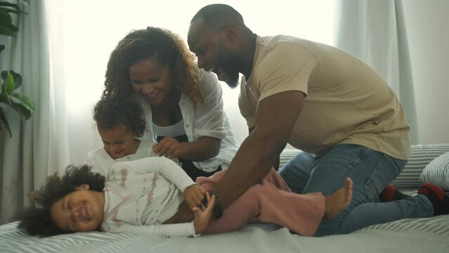 Happy African American Parents with  little daughters playing on the bed in bedroom at home, happy family concept
