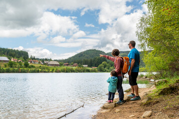 Mother, father and their little daughter at a lakeshore pointing Schluchsee village in Black Forest, Germany.