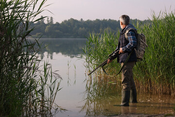 Man with hunting rifle near lake outdoors. Space for text