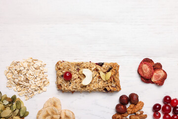 Tasty granola bar and ingredients on white wooden table, flat lay. Space for text