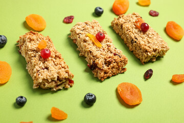 Tasty granola bars and ingredients on green table