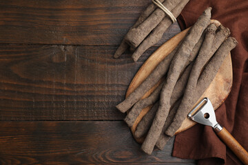 Raw salsify roots and peeler on wooden table, flat lay. Space for text