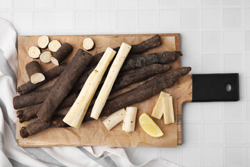 Raw salsify roots and lemon on white tiled table, top view