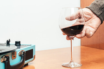 Horizontal photo senior adult hand holding glass of wine next to record player Concept hobbies art