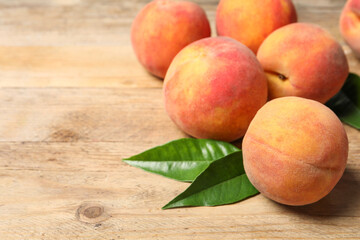 Fresh peaches and leaves on wooden table, closeup. Space for text