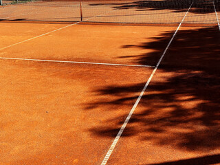 Wide view of classic orange outdoor tennis clay court with net, white lines and shadows. Fitness...