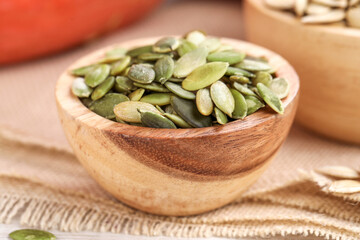 Wooden bowl with peeled pumpkin seeds on table, closeup