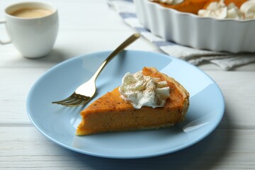 Piece of delicious pumpkin pie with whipped cream and fork on white wooden table, closeup