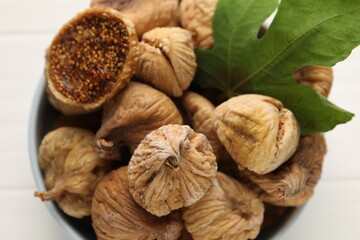Bowl with tasty dried figs and green leaf on white table, top view