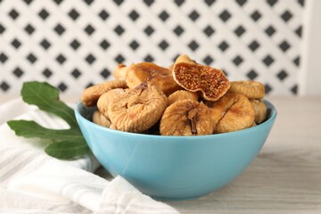 Bowl with tasty dried figs and green leaf on white wooden table, closeup