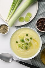 Bowl of tasty cream soup with leek and spoon on white wooden table, flat lay