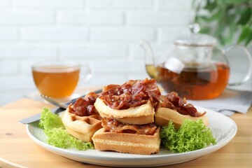 Tasty Belgian waffles served with bacon, lettuce and tea on wooden table, closeup
