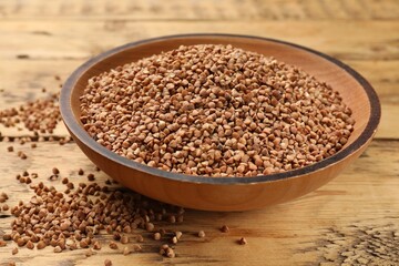 Bowl with dry buckwheat on wooden table, closeup