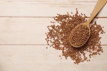 Spoon with dry buckwheat on light wooden table, top view. Space for text