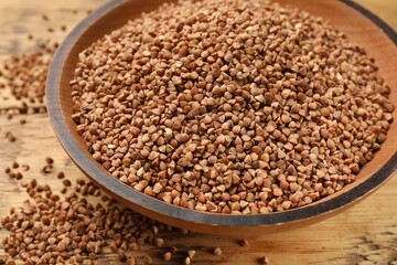 Bowl with dry buckwheat on wooden table, closeup