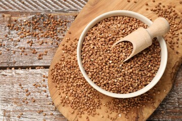Bowl and scoop with dry buckwheat on wooden table, top view. Space for text