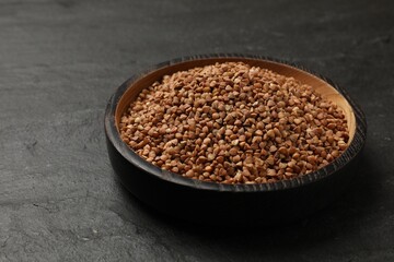 Bowl with dry buckwheat on black table. Space for text