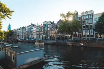 Fototapeta na wymiar Sunset illuminates a water canal and adjacent buildings in the capital city of Amsterdam, the Netherlands. Venice of the North