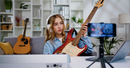 Beautiful preteen female blogger recording video class tutorial for play electric guitar on modern...