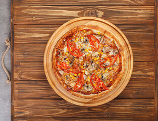 delicious pizza with chicken, mushrooms, cheese, tomatoes and corn on a wooden background