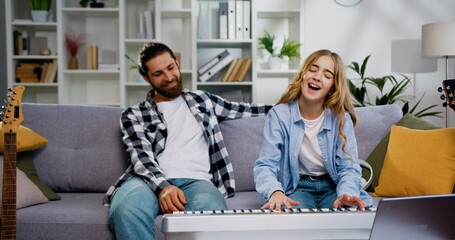 Lovely daughter play piano with father in the living room with happy moment. Child learning playing piano from her father. Weekend activity happy family lifestyle concept © serg