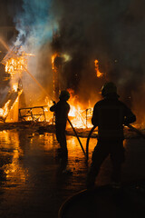 Two firefighters in action, fighting very strong fire, against light, dangerous, extinguishing fire
