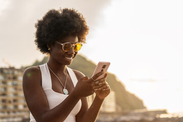 Trendy african woman using phone outdoors during sunset