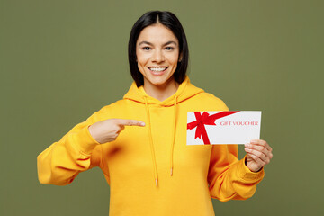 Young smiling Latin woman wears yellow hoody casual clothes hold point on gift certificate coupon voucher card for store isolated on plain pastel green background studio portrait. Lifestyle concept.