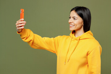 Young Latin woman she wear yellow hoody casual clothes doing selfie shot on mobile cell phone post photo on social network isolated on plain pastel green background studio portrait. Lifestyle concept