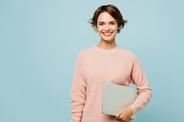 Young fun smiling happy IT woman she wears beige knitted sweater casual clothes hold closed laptop...