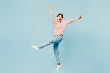 Full body side view young woman she wear beige knitted sweater casual clothes listen to music in headphones raise up hands leg isolated on plain pastel light blue cyan background. Lifestyle concept.