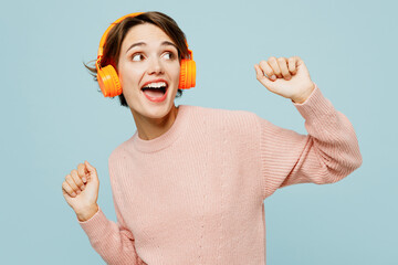 Young fun cool woman wear beige knitted sweater casual clothes listen to music in headphones dance...