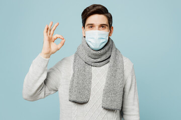 Young ill sick man wearing gray sweater scarf sterile face mask show ok okay isolated on plain blue...