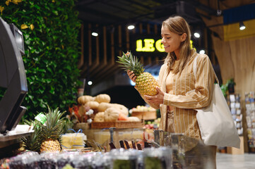 Young customer woman wearing casual clothes hold pine-apple shopping with shopper bag at supermaket store grocery shop buying fruit choose products in hypermarket. Purchasing food gastronomy concept. - Powered by Adobe