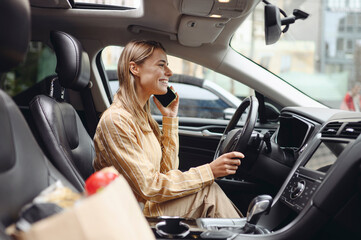 Young customer woman wear casual clothes speak mobile cell phone driving car with paper bag of...