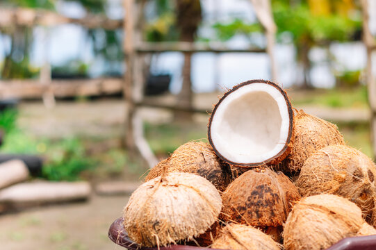 Horizontal image of a group of fresh coconuts stacked in a basket with an out of focus background of a tropical Caribbean beach with copy space on the left. Concept of natural food.