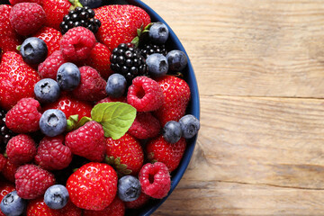 Different fresh ripe berries in bowl on wooden table, top view. Space for text