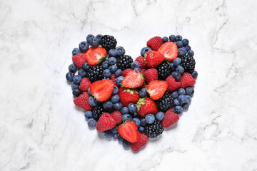Heart made of different fresh ripe berries on white marble table, top view