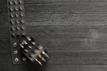 Black studded leather bracelet on the black wooden table background close up.