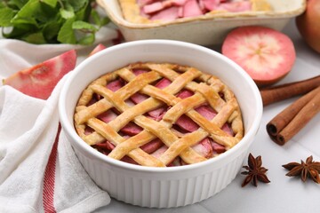 Baking dish with delicious apple pie and ingredients on white tiled table
