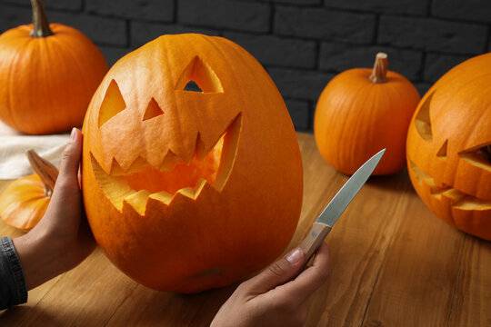 Woman with carved pumpkins and knife at wooden table, closeup. Halloween celebration
