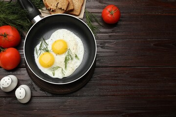 Frying pan with tasty cooked eggs, dill and other products on wooden table, flat lay. Space for text