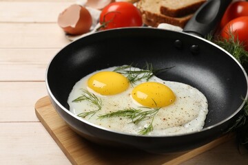 Frying pan with tasty cooked eggs, dill and other products on light wooden table, closeup