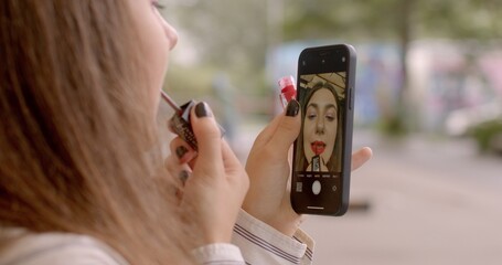 Using a phone as mirror. Lip makeup. Applying Lipstick Using the Front-Facing Camera on a smartphone. People appearance on the go lifestyle. Integration of technology into everyday life woman portrait