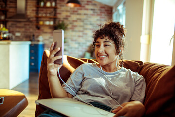 Joyful woman enjoying music while browsing on her smartphone at home