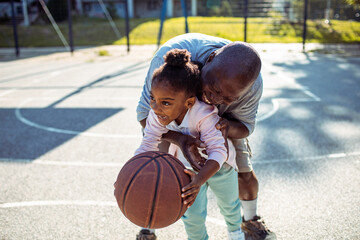 Grandfather playfully teaches his granddaughter how to handle a basketball