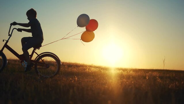 boy on a bicycle. happy family kid dream concept. a boy rides a bicycle with balloons along the road of a large field under the rays of the sun. boy in shorts and a T-shirt rides bicycle lifestyle