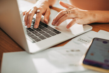 Person efficiently multitasking on a laptop, with paperwork and a smartphone nearby